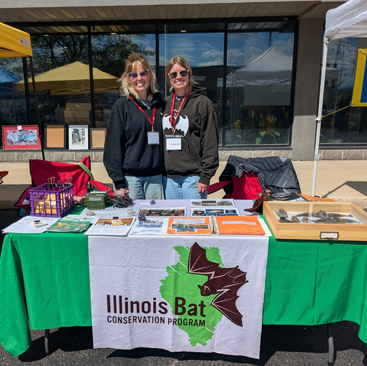 Abby and Brittany behind table with outreach materials and green tablecloth
